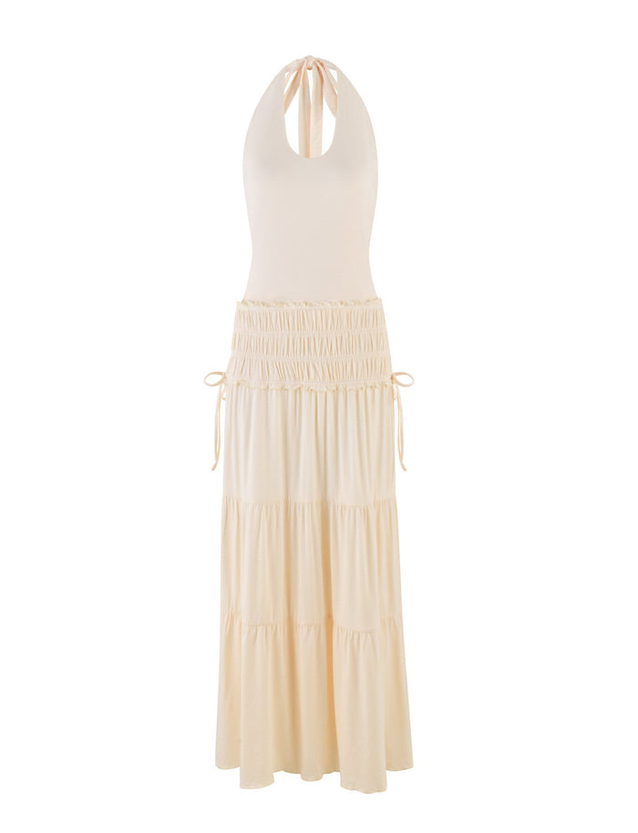 The TIGERMIST DENALI HALTER DRESS in Bone is a cream-colored maxi with a fitted sleeveless bodice, keyhole neckline, tiered skirt, adjustable side waist ties, and a soft, flowing silhouette in buttery jersey.