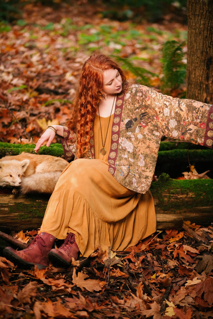 Model wearing Dreamweaver Matinée Duster featuring Alphonse Mucha’s 1896 zodiac woman – trimmed with celestial symbols on deep burgundy background – Market of Stars.