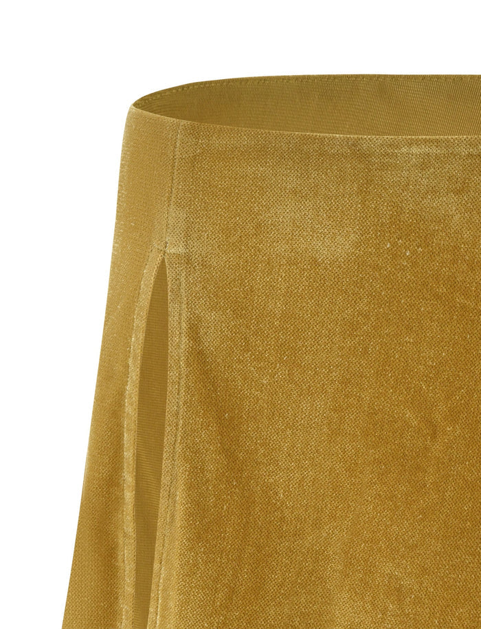 Close-up of the golden-yellow velvet fabric of the HARLOWE SKIRT - GOLD by TIGERMIST. The material has a soft, rich texture with a subtle sheen and slight draped flow. A seam with a slit detail is visible against the white background.
