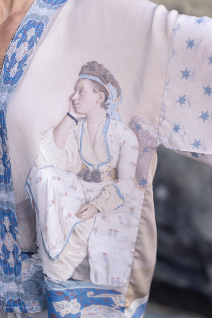 Model wearing the Head in the Clouds Opera Duster featuring Liotard’s portrait of his wife with Turkish textiles, starry sleeves, and poetic script – Market of Stars.