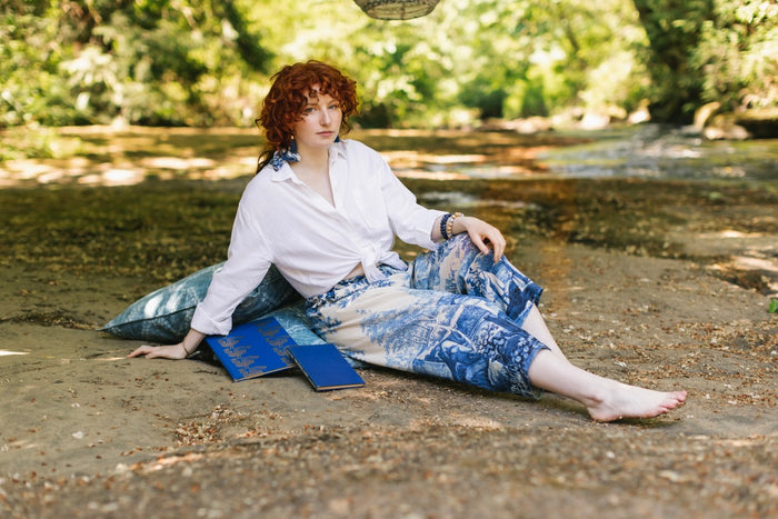 Model wearing Let the Light In linen Artist Pant featuring print of Delft blue and white landscape pottery, and positive message of light and hope - Market of Stars