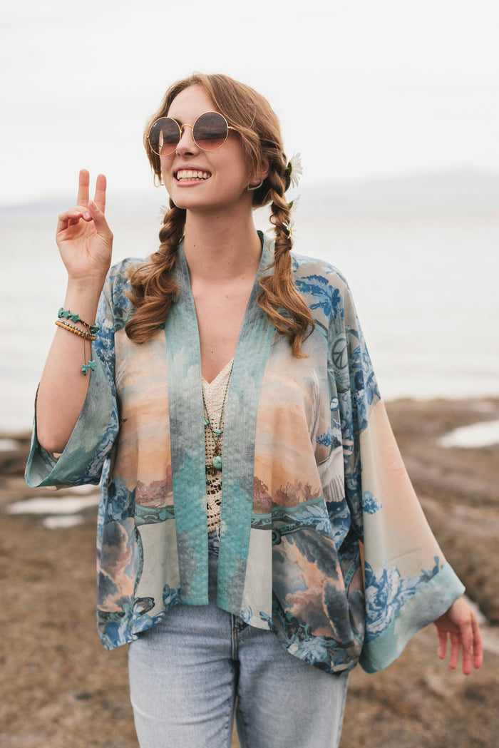 Model wearing our Peace Out Pixie Duster featuring 1800's perfumeur sign with gentle tones of blue & aqua, landscapes, clouds, dove and peace symbols -Market of Stars.