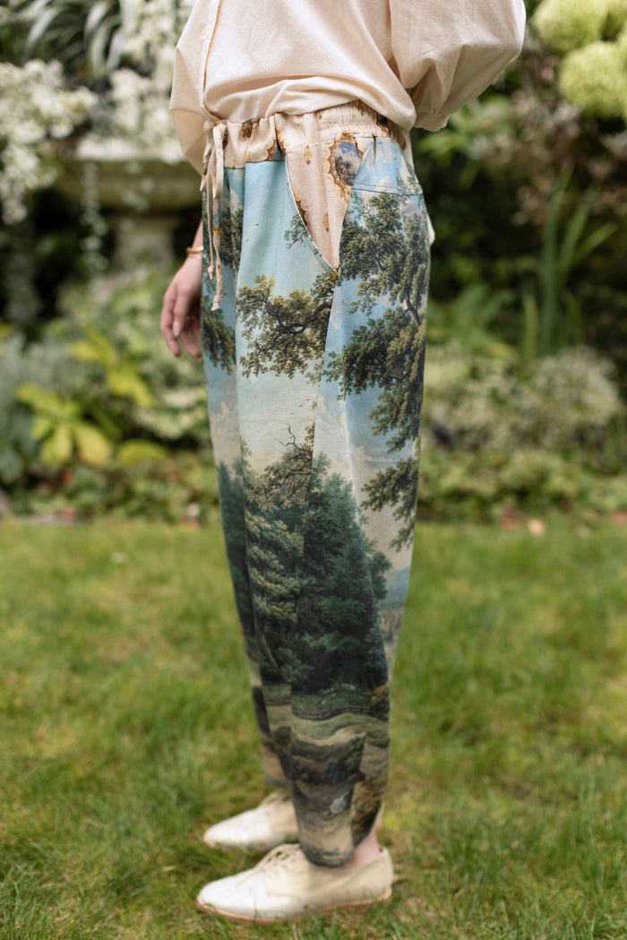 Model wearing a cropped length linen blend pant ft. vintage artwork & unicorn lorn set against a mossy-green landscape — a romantic piece for the modern dreamer - Market of Stars