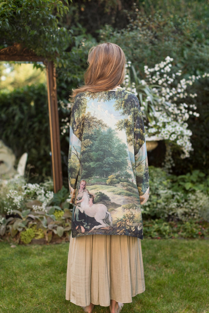 Model wearing a mid-length duster ft. vintage artwork & unicorn lorn set against a mossy-green landscape — a romantic piece for the modern dreamer - Market of Stars