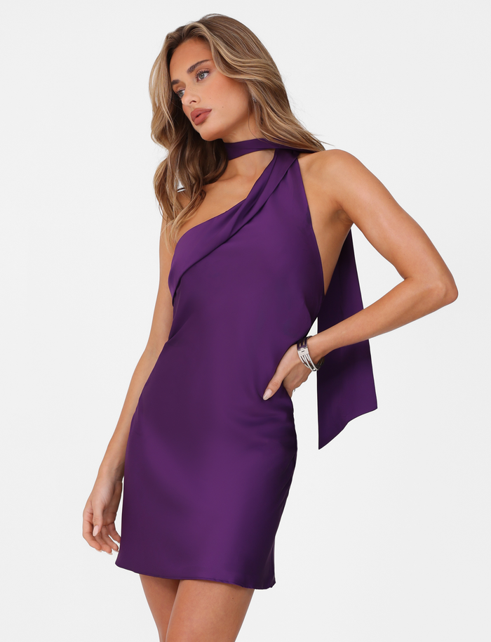 A woman poses confidently with one hand on her hip, wearing the TIGERMIST ALLIRA MINI DRESS 2.0 in Lavender (Purple) satin against a white background, looking to the side.