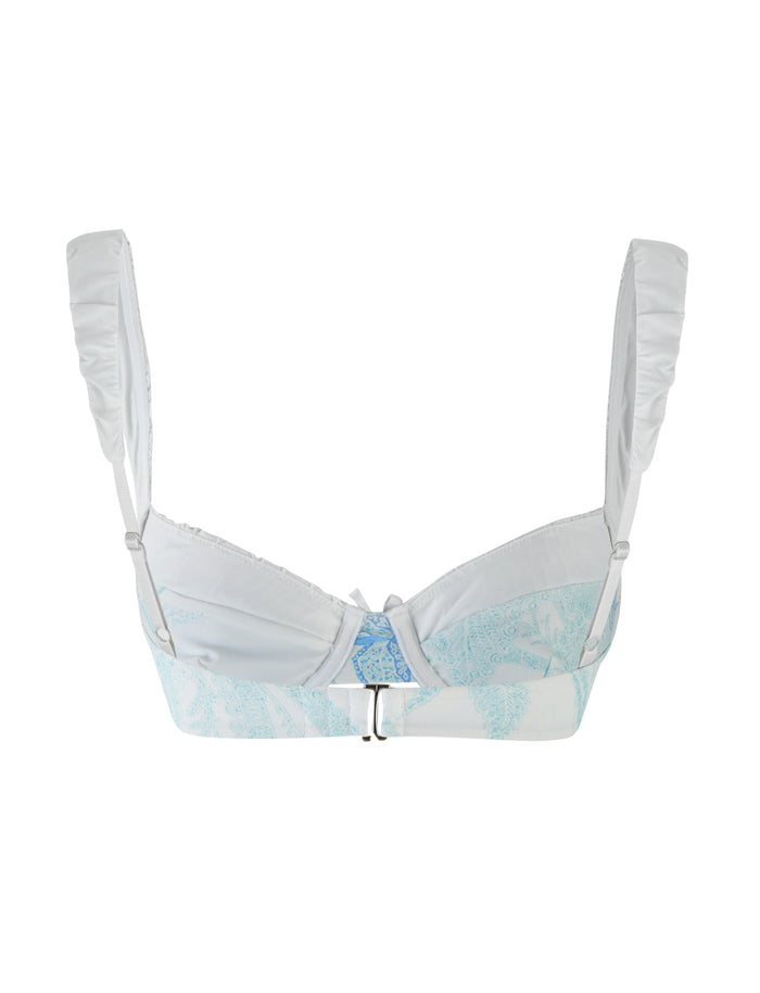 The AMARAN BIKINI TOP - BLUE : FLORAL TAPESTRY by TIGERMIST is a light blue lace balconette bikini top featuring intricate floral patterns. It comes with adjustable straps and a front closure, set against a plain white background.