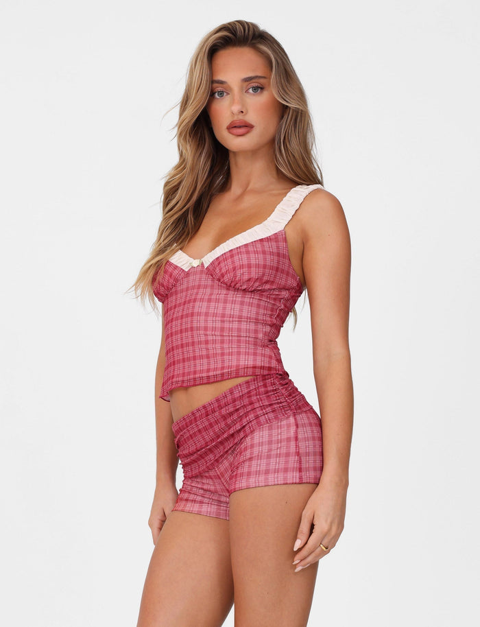 Against a plain white backdrop, a woman with long hair poses in a TIGERMIST RED CHECK outfit, featuring an Amaran Top with ruffled straps.