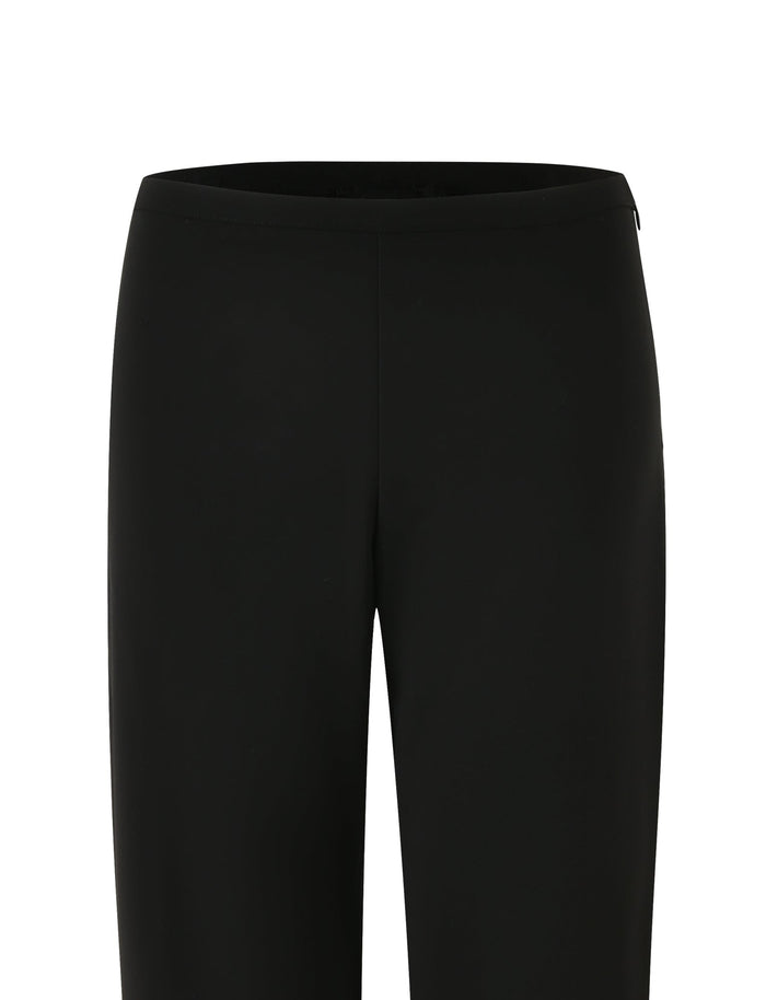 A close-up of the TIGERMIST AUDRIE PANT - BLACK is shown from the waistband to the knees, set against a plain white background. The pants have a smooth, sleek finish and appear to be made of formal suiting fabrication. There are no visible pockets or belt loops.