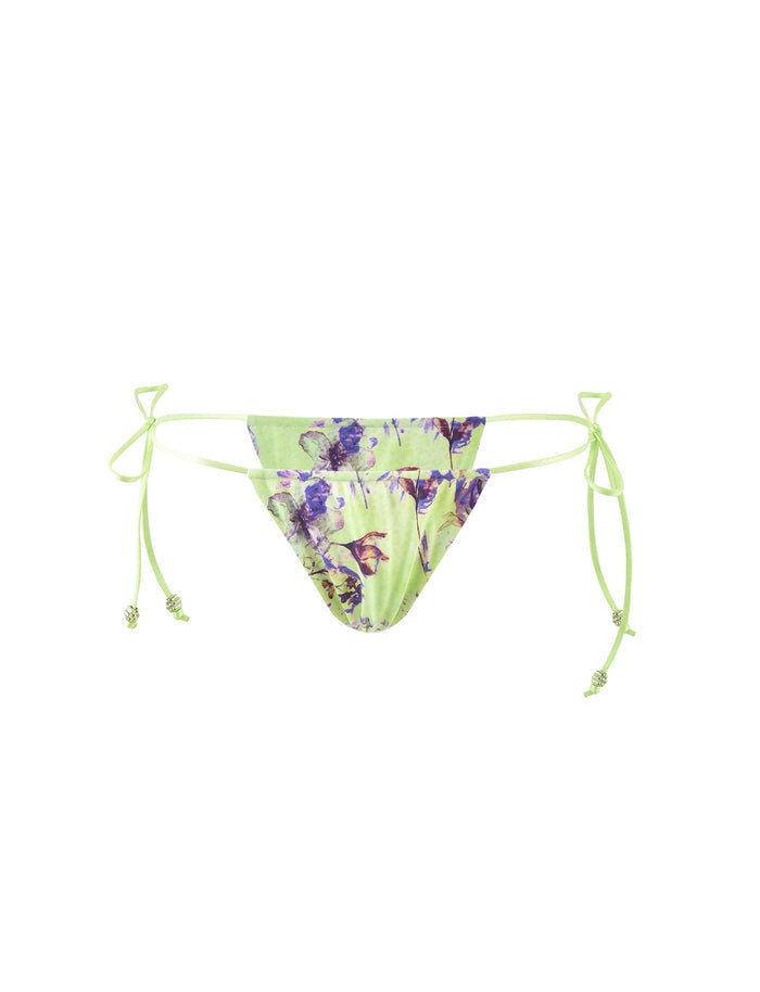 The AVE Bikini Bottom in Green by Poppy Floral from TIGERMIST features a chic design with side ties on a white background. The fabric is adorned with purple and pink floral patterns, and the ties include small knotted details, embodying the signature style of the brand.