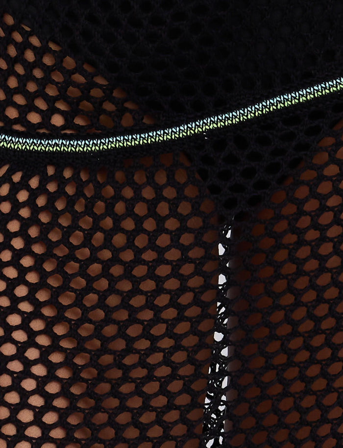Close-up image of the AZARIA SKIRT - BLACK by TIGERMIST, showcasing its black fishnet mesh fabric adorned with visible white and green stitching. The background features a darker, shadowed area that emphasizes the skirt's intricate texture and pattern, embodying Tiger Mist's edgy aesthetic.