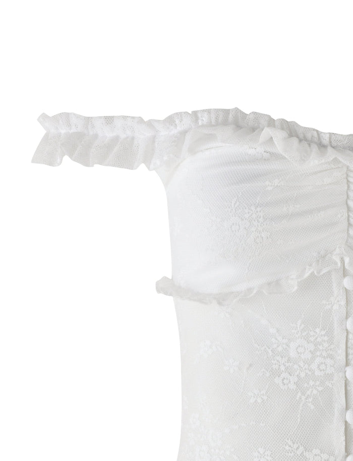 Close-up of the BENTON TOP - WHITE from TIGERMIST. This off-the-shoulder design features intricate lace detailing and a ruffled trim along the neckline. The sheer mesh bodice is adorned with buttons running down the side, adding an elegant touch to the garment. The top appears delicate and bridal-inspired.