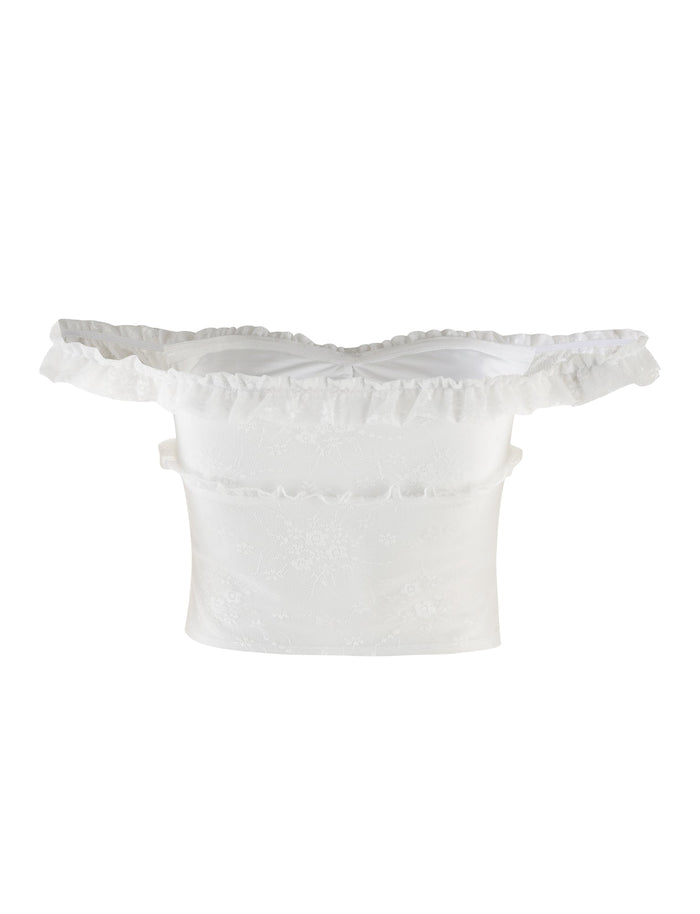 The BENTON TOP - WHITE by TIGERMIST is a strapless, off-the-shoulder top featuring ruffled details along the neckline. It has a subtle floral pattern and a sheer mesh bodice that fits snugly around the waist.