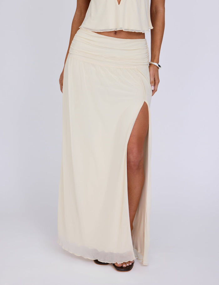 A person wearing a flowing, light cream Tiger Mist Birdee Skirt with a thigh-high slit on the side, standing against a plain white background. The skirt is paired with a matching crop top, and a bracelet is visible on the person's left wrist.