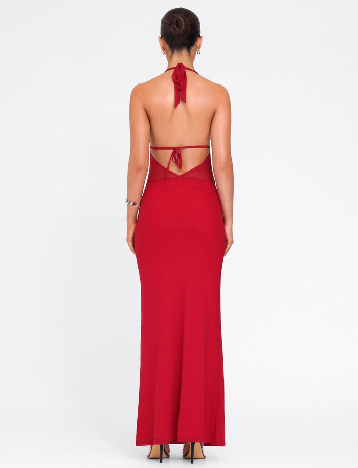 A woman with her hair up wears the TIGERMIST BRESILY MAXI DRESS in red—a long, backless halter style tied at the neck and mid-back. She pairs it with high heels and hoop earrings against a plain white background.