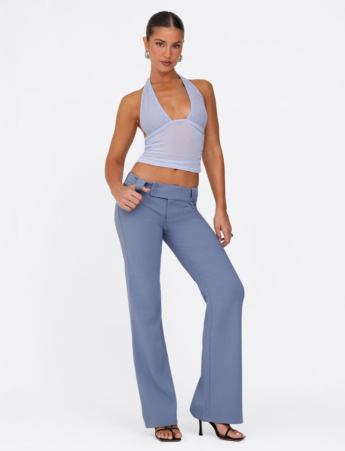 A person poses confidently in a stylish ensemble, wearing the TIGERMIST BRESILY Top in Steel Blue alongside high-waisted flared pants. Hoop earrings and black high-heeled sandals complete the look as they stand against a plain white background.