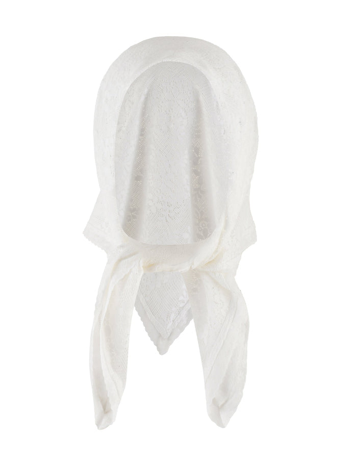 A woman wearing the BRIONY SCARF in white by TIGERMIST and a brown ruched mini skirt stands against a plain background. She has long, dark hair and is accessorizing with rings and a bracelet. Her left hand, adjusting her skirt, highlights the intricate lace fabrication of her outfit.