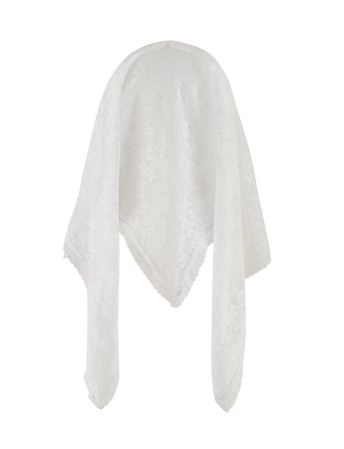 A woman is standing against a plain white background. She is wearing a white strapless top with an asymmetrical hem, complemented by a dark brown mini skirt. Her long dark hair cascades over her shoulders, and she sports high-heeled sandals. Around her neck drapes the elegant BRIONY SCARF - WHITE crafted from delicate lace fabrication by TIGERMIST.
