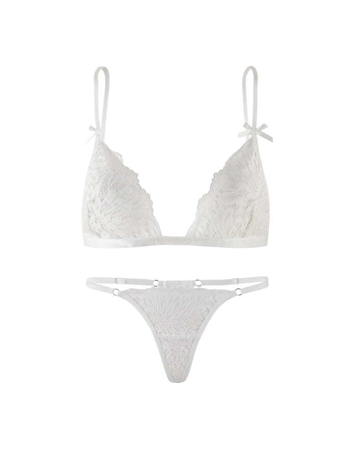 A delicate intimate set from TIGERMIST, the BROOKE SET - WHITE features a sheer lace bralette with adjustable shoulder straps and matching lace panties. The bralette is adorned with a floral design, while the panties include side straps with small metal rings connecting to the lace portion.