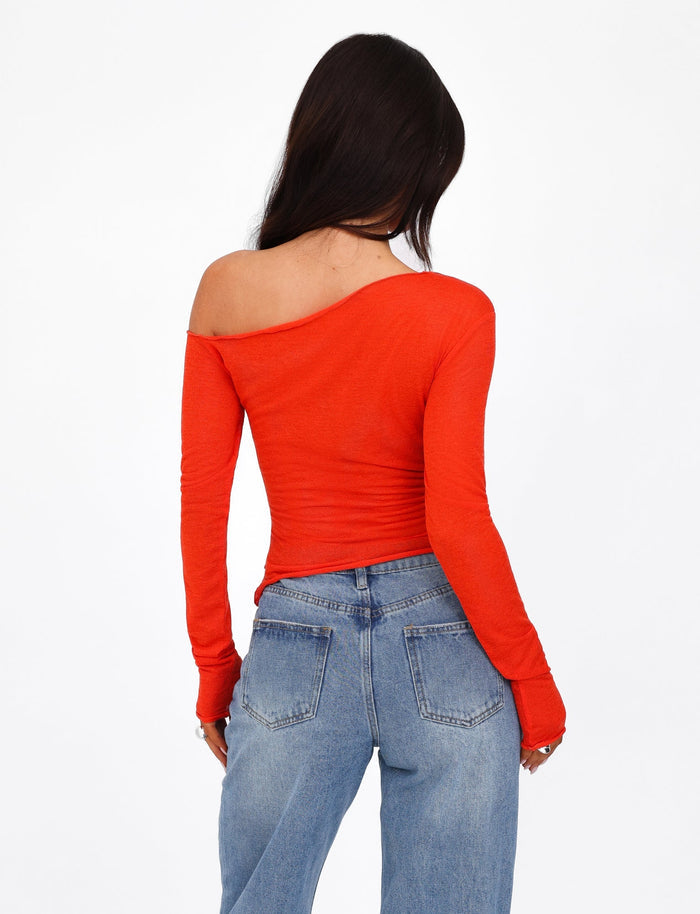 A person with long dark hair is standing with their back to the camera, showcasing the TIGERMIST BRYNA JUMPER in red, an off-the-shoulder, long-sleeve knit sweater paired with high-waisted blue jeans. The background is plain white.