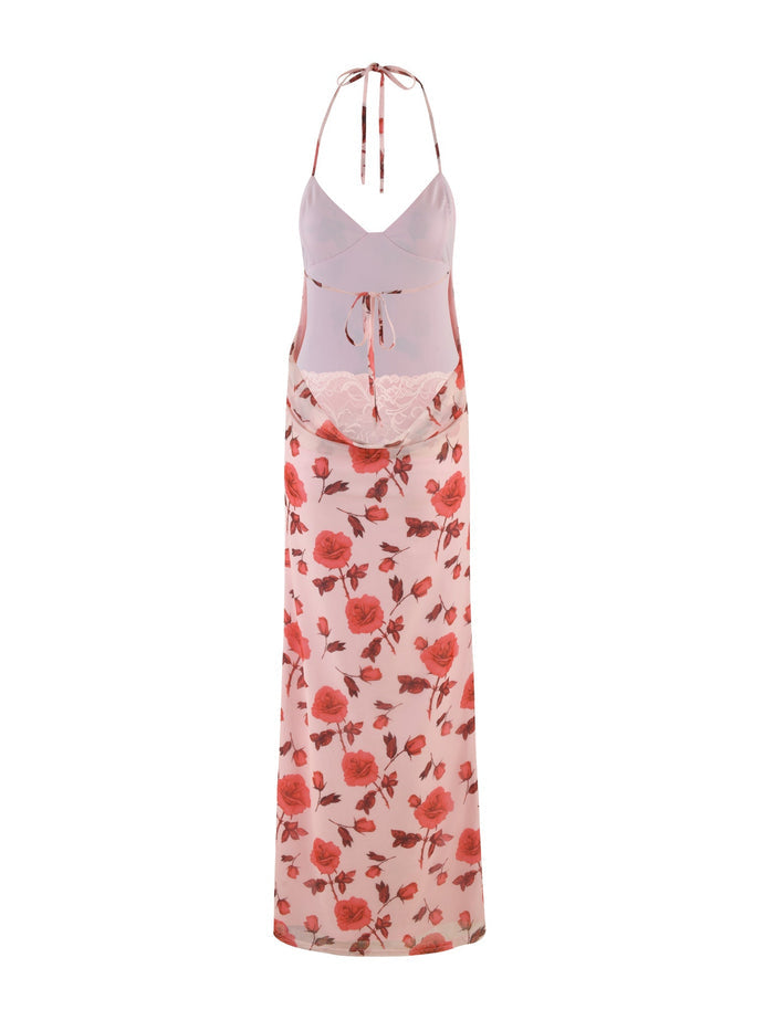 The BRYSTOL DRESS - RED : FLORAL by TIGERMIST is a long, sheer white dress adorned with a pattern of pink and red roses. It features a deep V-neck, a tie closure, and delicate lace detailing at the waist. This maxi-length dress boasts a halter neckline and an open back design for an elegant appearance.