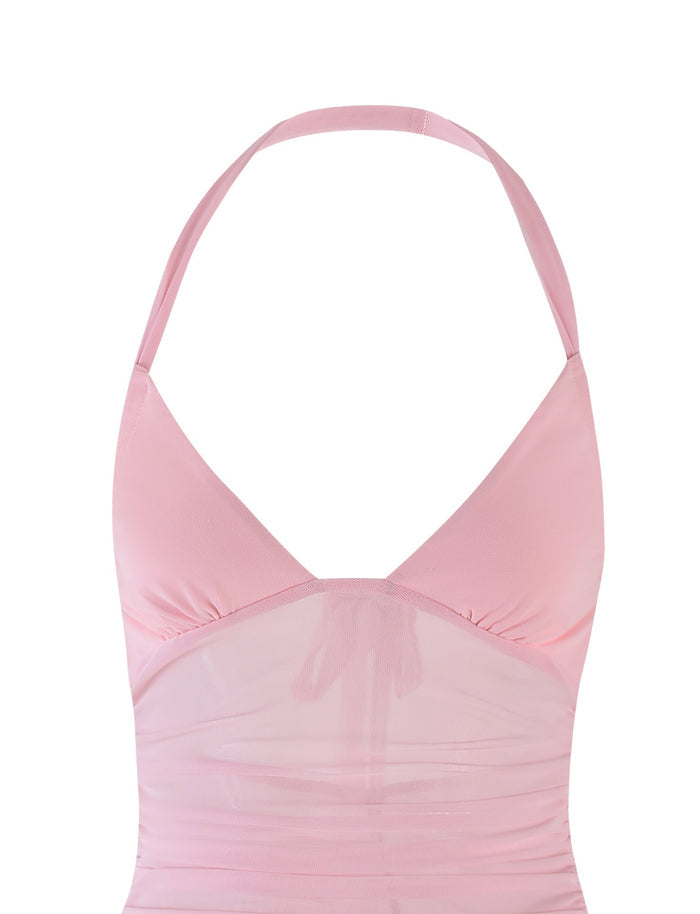 The CARMELA DRESS - PINK by TIGERMIST is a baby pink halter-neck cropped top crafted from sheer, lightweight material. It boasts a slightly gathered fabric under the bust to create a ruched effect and features a thin strap that ties around the neck, offering a chic and effortlessly stylish appearance.