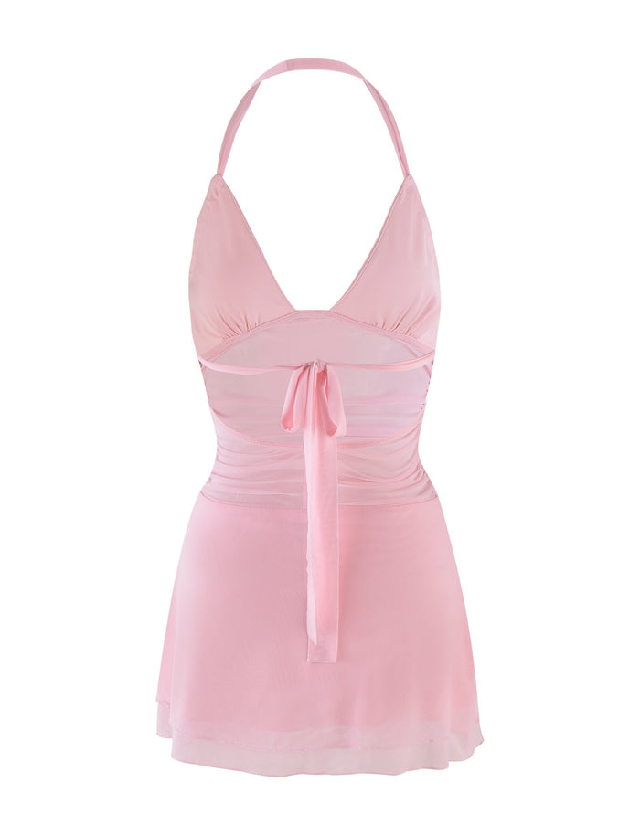 The CARMELA DRESS in baby pink by TIGERMIST features a halter-neck design with a fitted bodice and tie detail at the front, complemented by a flared skirt and a slightly sheer waist panel, creating an elegant and feminine look.