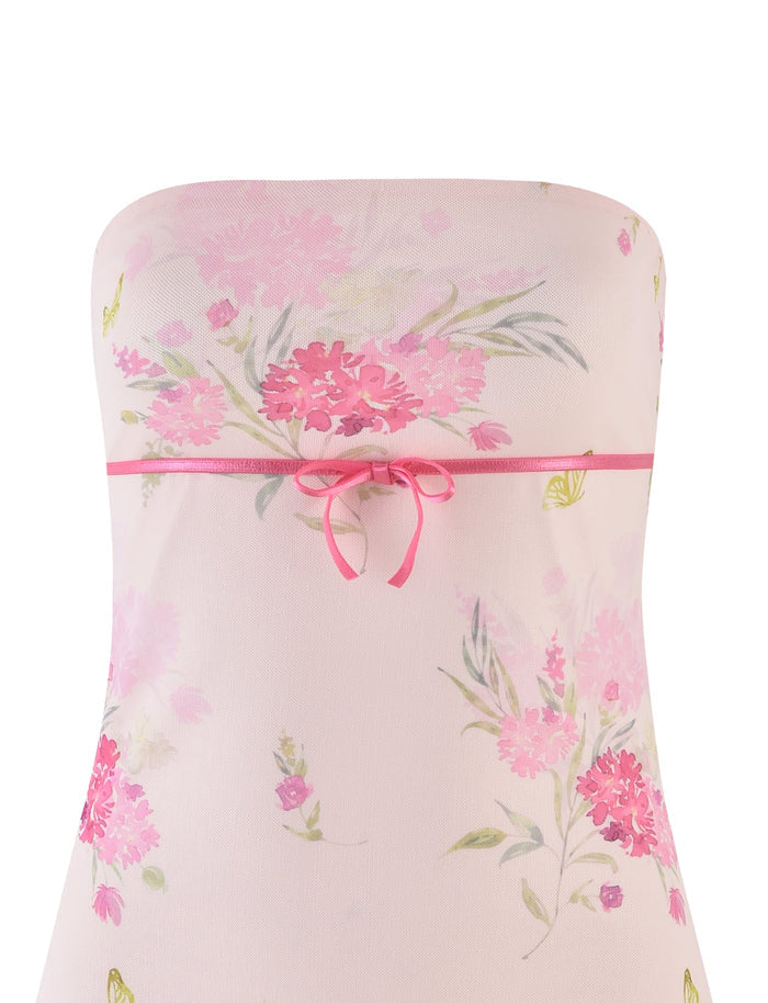 The CARSYN MINI DRESS by TIGERMIST features a watercolor floral print in pink and green. It is designed with a strapless neckline, an asymmetrical hemline, and cinched at the waist with a pink ribbon bow.