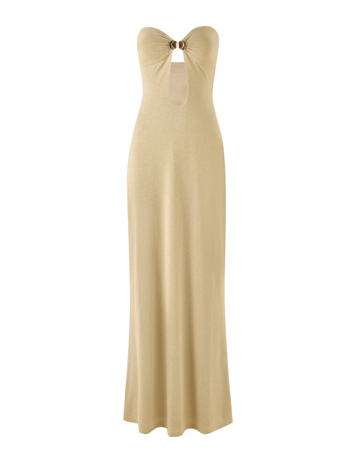 The TIGERMIST CECILY MAXI DRESS - GOLD showcases a long, strapless design in a beige gold colourway, featuring a central ring detail at the neckline that forms a keyhole cutout at the chest. The dress boasts a sleek and smooth silhouette that extends to the floor.