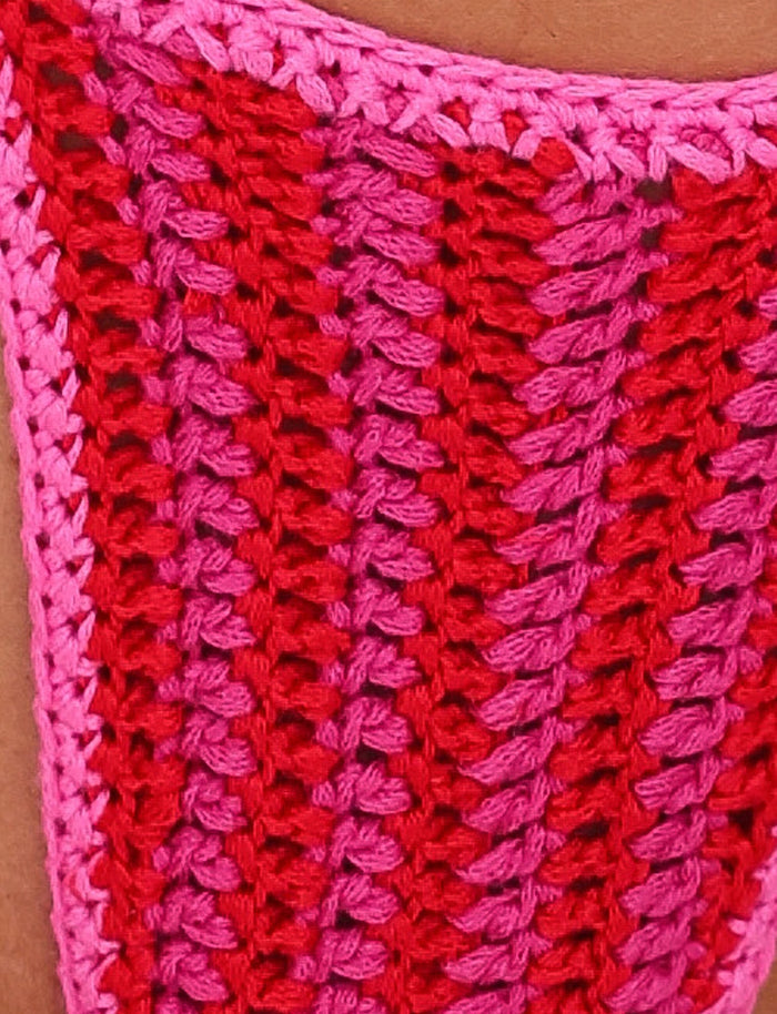 Close-up of a crocheted fabric piece featuring a vibrant pattern. The TIGERMIST CORA BIKINI BOTTOM - PINK : STRIPE alternates between bright pink and red vertical stripes, showcasing the playful design of a cheeky bikini cut and creating a textured, woven appearance.
