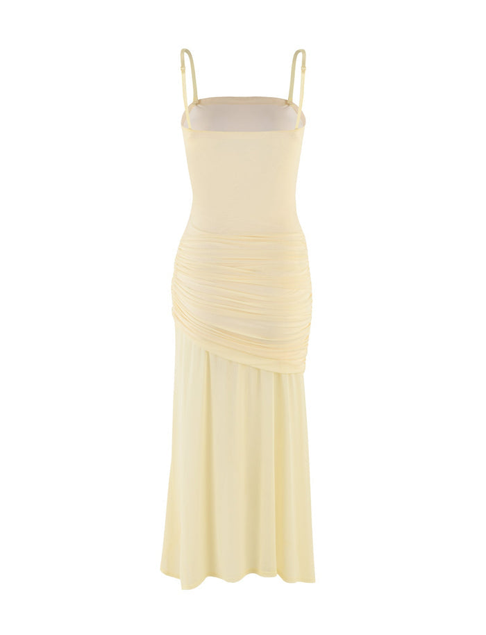 This COVE MIDI DRESS - YELLOW : BUTTER by TIGERMIST showcases a sleeveless design with thin straps and ruched detailing at the waist. The fabric drapes elegantly to create a flowing silhouette, ending in an asymmetric hem that adds flair.