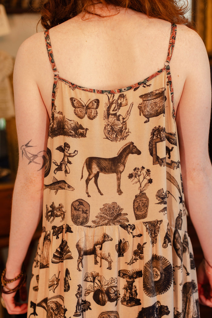 Model wearing a maxi-length bamboo viscose slip dress inspired by a mysterious Victorian scrapbook. This whimsical print celebrates the wonder hidden in ordinary things — Market of Stars.
