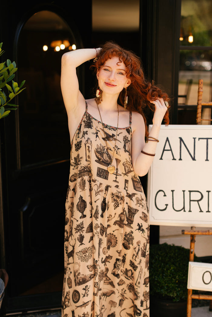 Model wearing a maxi-length bamboo viscose slip dress inspired by a mysterious Victorian scrapbook. This whimsical print celebrates the wonder hidden in ordinary things — Market of Stars.