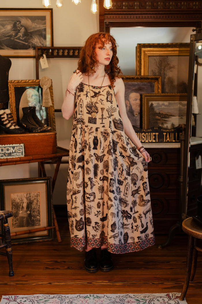 Model wearing a maxi-length bamboo viscose slip dress inspired by a mysterious Victorian scrapbook. This whimsical print celebrates the wonder hidden in ordinary things — Market of Stars.