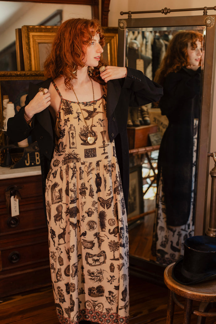 Model wearing a maxi-length bamboo viscose slip dress inspired by a mysterious Victorian scrapbook. This whimsical print celebrates the wonder hidden in ordinary things — Market of Stars.