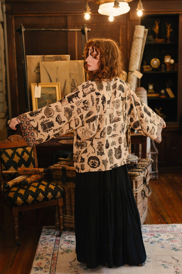 Model wearing a bamboo-viscose cropped length duster inspired by a mysterious Victorian scrapbook. This whimsical print celebrates the wonder hidden in ordinary things — Market of Stars.