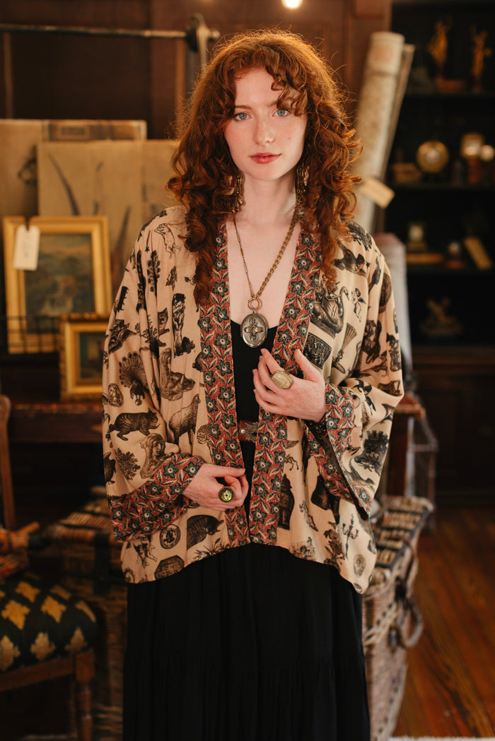 Model wearing a bamboo-viscose cropped length duster inspired by a mysterious Victorian scrapbook. This whimsical print celebrates the wonder hidden in ordinary things — Market of Stars.
