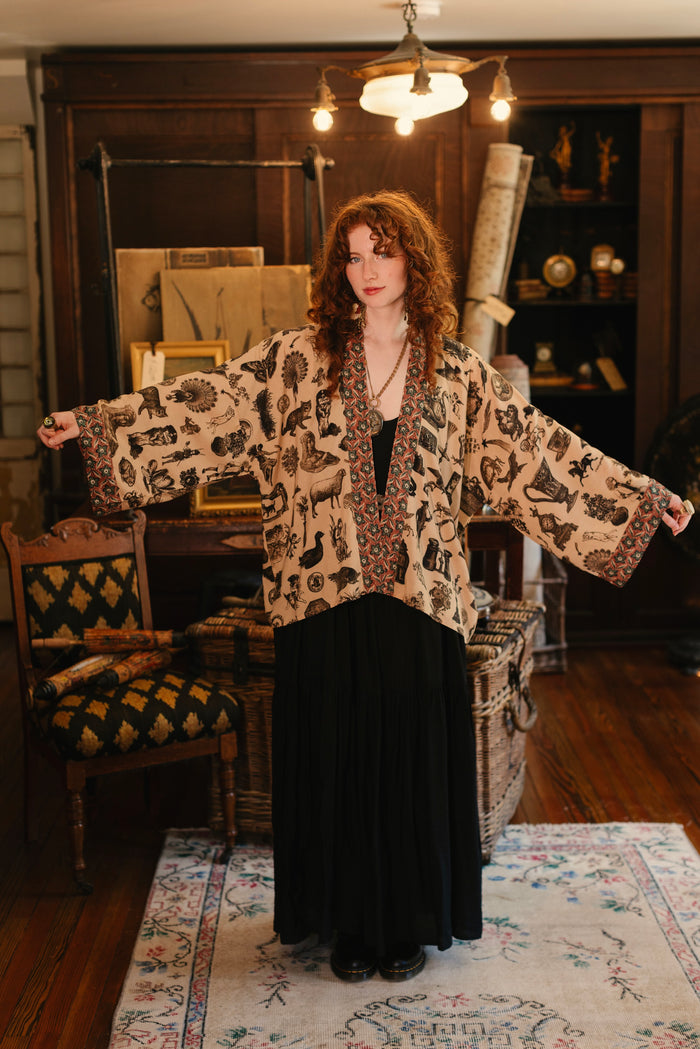 Model wearing a bamboo-viscose cropped length duster inspired by a mysterious Victorian scrapbook. This whimsical print celebrates the wonder hidden in ordinary things — Market of Stars.