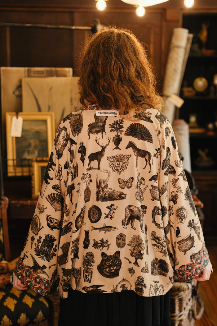 Model wearing a bamboo-viscose cropped length duster inspired by a mysterious Victorian scrapbook. This whimsical print celebrates the wonder hidden in ordinary things — Market of Stars.
