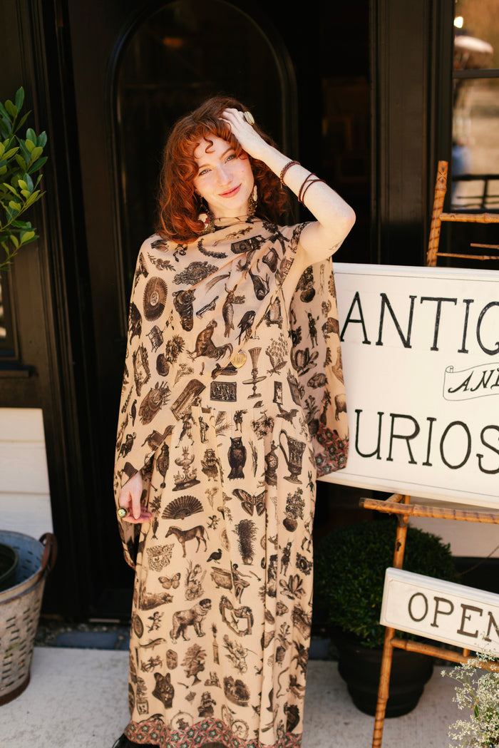 Model wearing a bamboo-viscose scarf inspired by a mysterious Victorian scrapbook. This whimsical print celebrates the wonder hidden in ordinary things — Market of Stars.