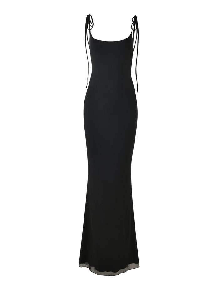 The CYRIL DRESS - BLACK by TIGERMIST is a long, elegant dress with adjustable shoulder straps tied into bows. It features a form-fitting design that flares slightly at the bottom, creating a graceful silhouette. Displayed on a white background, it emphasizes the simplicity and sophistication of its black colourway.