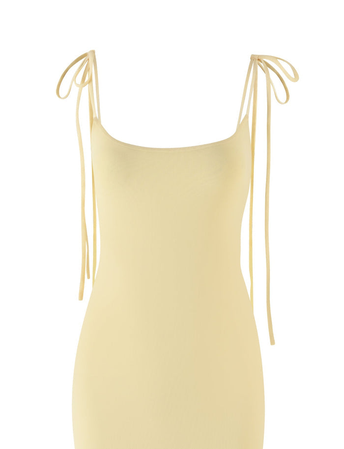 The CYRIL DRESS - YELLOW : LEMON by TIGERMIST is a pale yellow maxi dress with thin, adjustable spaghetti straps that tie in bows at the shoulders. Its minimalist design and smooth texture extend elegantly downward without any additional patterns or embellishments, complemented by a satin cowl back for added sophistication.