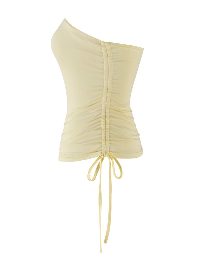 The DARIAN TOP - YELLOW : BUTTER by TIGERMIST is a light yellow, one-shoulder top featuring gathered ruching down the center front. Made from high stretch fabric, this fitted design includes a lace-up tie detail at the bottom.