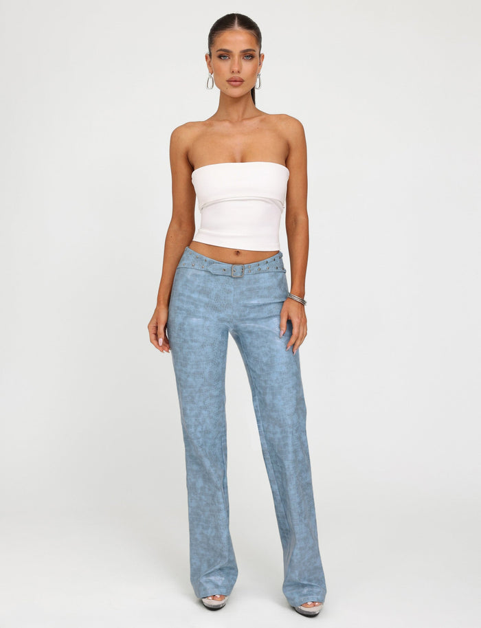 A woman stands against a plain white background, wearing the TIGERMIST DARIELLE TOP - WHITE and high-waisted light blue jeans from Tiger Mist. She has her hair pulled back and is accessorized with hoop earrings and bracelets. She looks directly at the camera with a neutral expression.