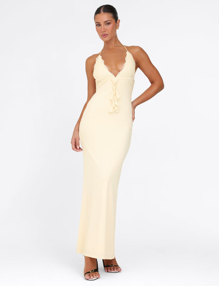 Someone showcases the DEENA MAXI DRESS - YELLOW : LEMON by TIGERMIST, an eye-catching maxi-length dress in light yellow. It boasts a deep V-neckline with intricate gathered details at the front and is beautifully adorned with elegant lace bust cups. They pose confidently in heeled sandals against a plain white backdrop.