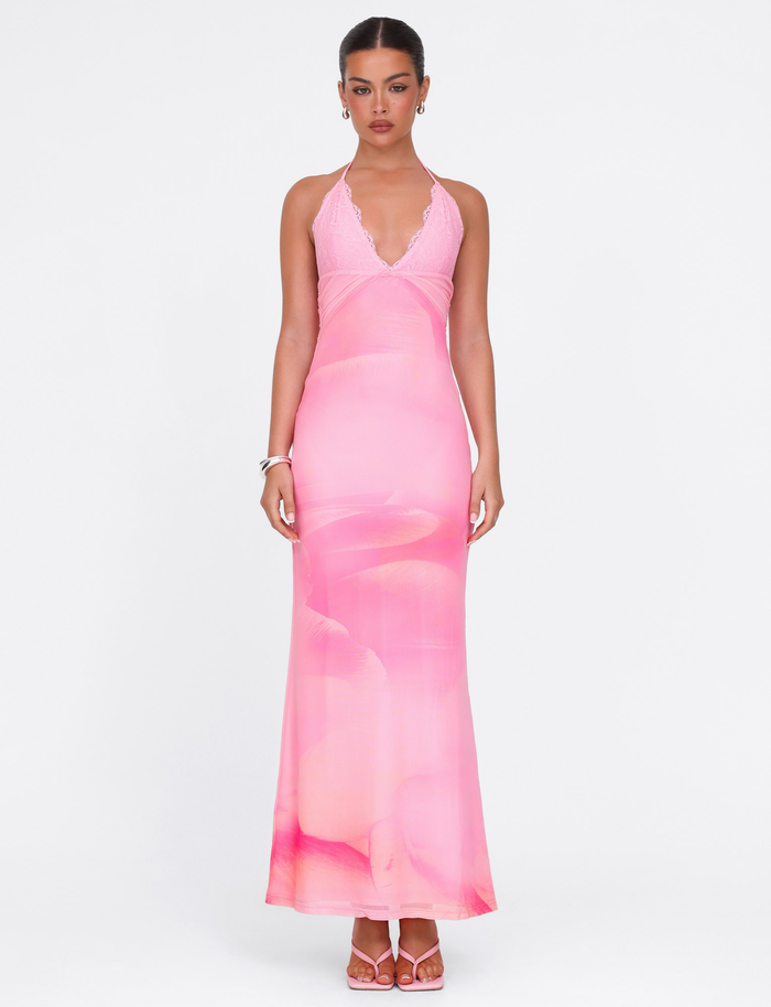 A woman poses against a white background in the TIGERMIST DENAE Maxi Dress - Pink Blossom, a form-fitting floral halter dress styled with pink heels and minimal jewelry.