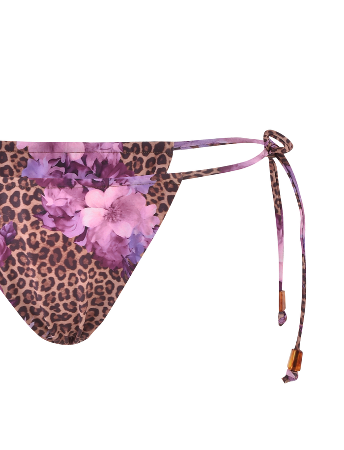 The TIGERMIST DESIRAE Bikini Bottom in Purple features a bold floral leopard print, adjustable side ties with purple straps, and wooden bead details.