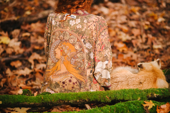 Model wearing Dreamweaver Matinée Duster featuring Alphonse Mucha’s 1896 zodiac woman – trimmed with celestial symbols on deep burgundy background – Market of Stars.