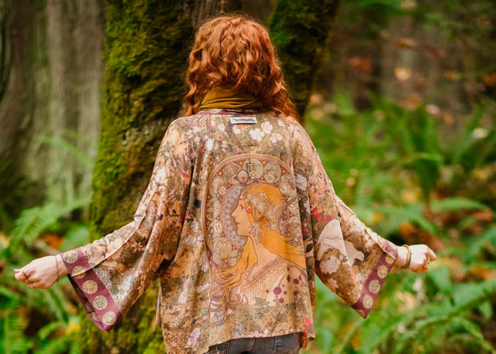 Model wearing Dreamweaver Matinée Duster featuring Alphonse Mucha’s 1896 zodiac woman – trimmed with celestial symbols on deep burgundy background – Market of Stars.