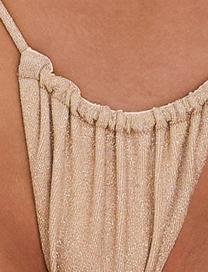 Close-up of the ELLISON BIKINI BOTTOM in gold from TIGERMIST with gathered details and a thin strap over a person's shoulder. The material appears soft and light, creating gentle folds.