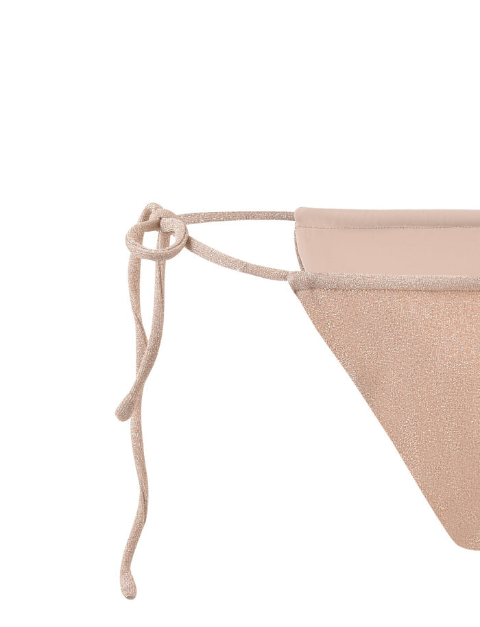 Close-up of the ELLISON BIKINI BOTTOM - GOLD by TIGERMIST with a minimalist aesthetic. It features a side tie knot made of the same gold material, creating a subtle, elegant look. The fabric appears to have a slight shimmer or metallic finish. The photo focuses on the tying detail.